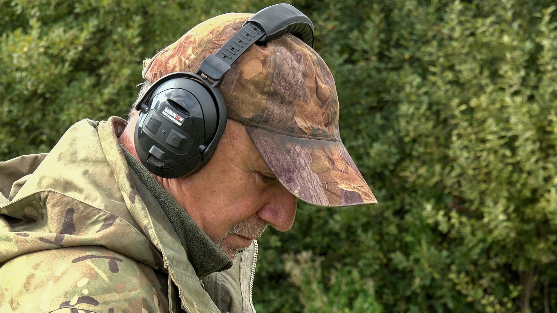 man in camouflage wearing headphones while metal detecting