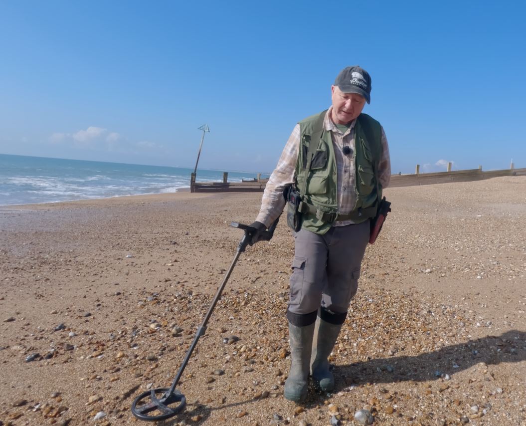 Man metal detecting on a beach with blue sky